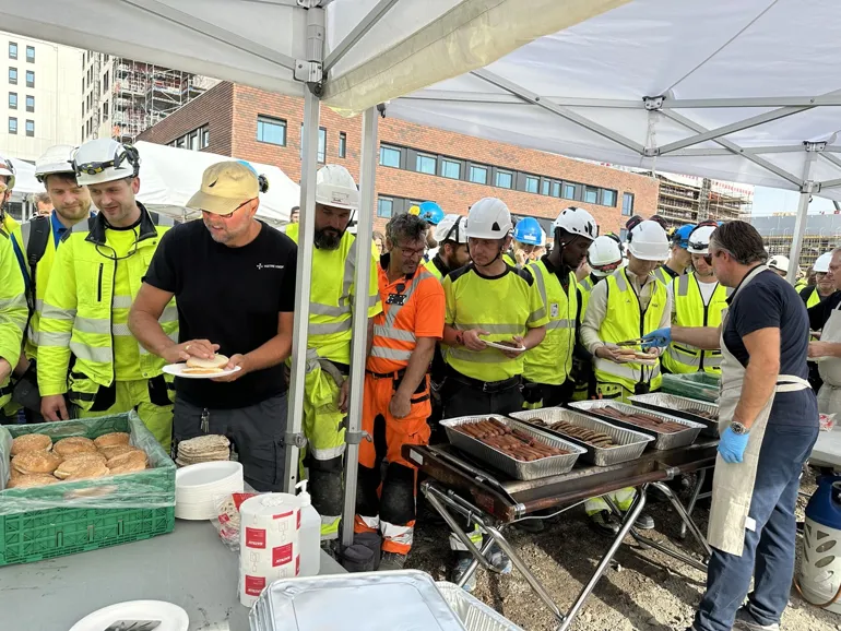 A group of people wearing safety vests and hats standing around a grill